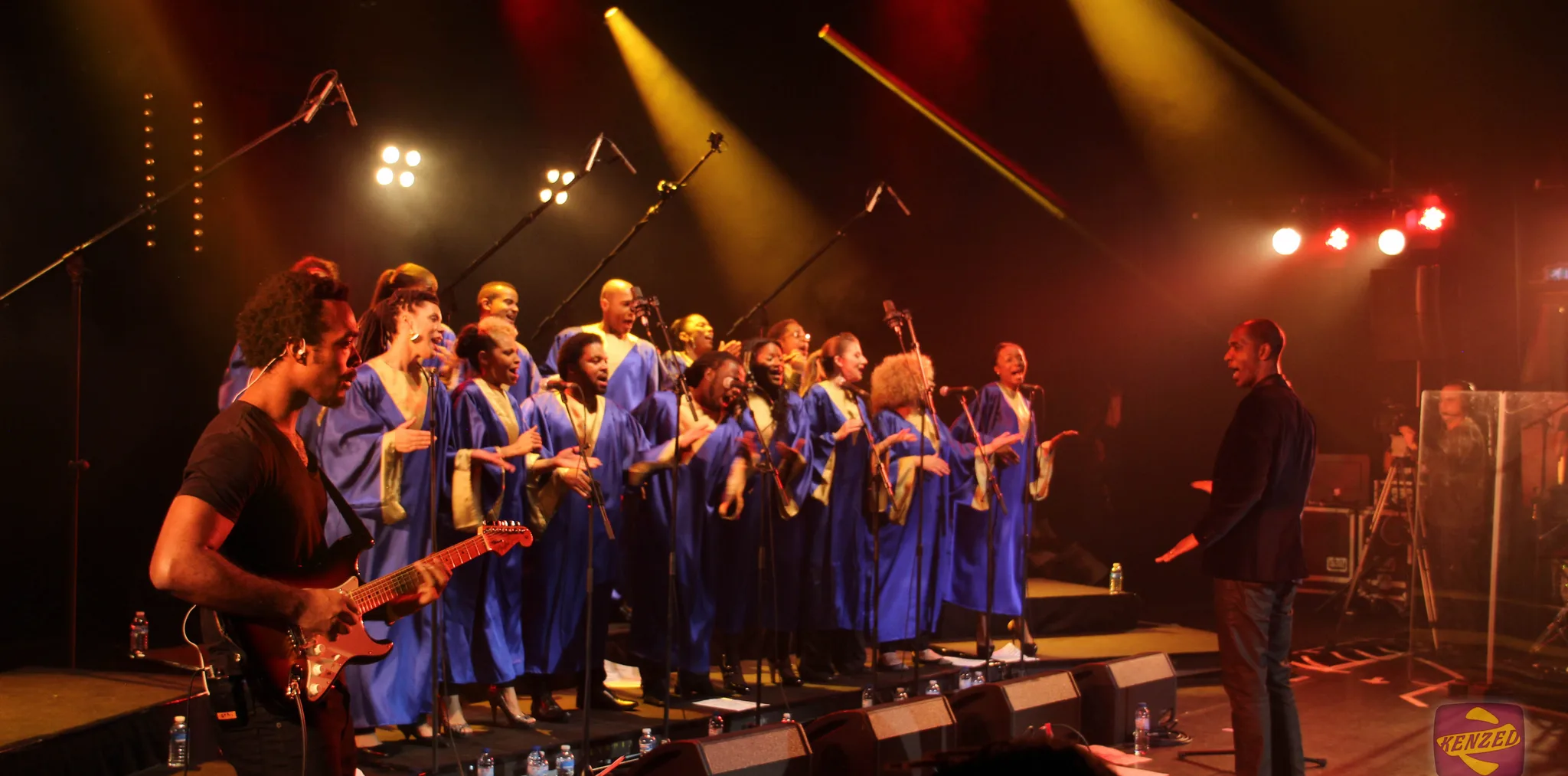 Max Zita dirige Gospel Voices sur scène, chœur en robes bleues sous les projecteurs