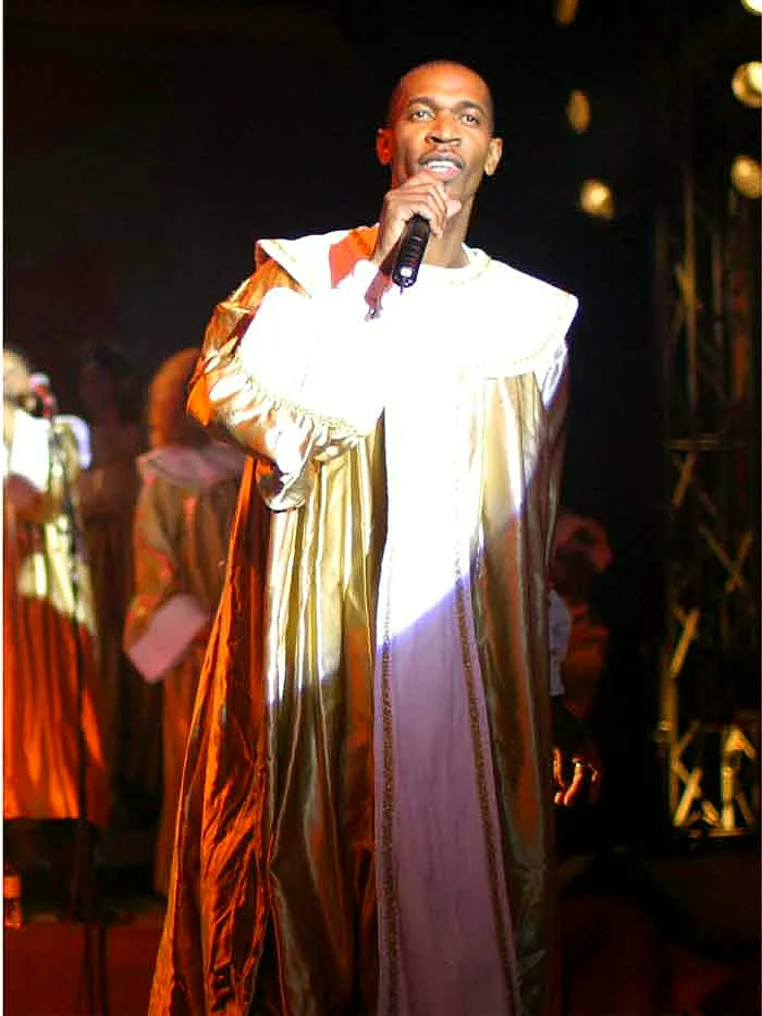Max Zita dirige Gospel Voices sur scène, chœur en robes bleues sous les projecteurs